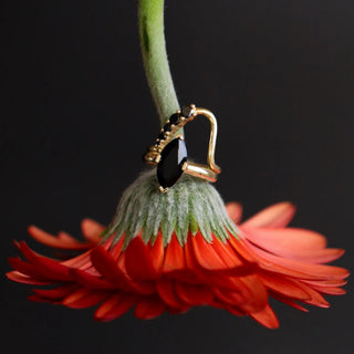 upside down flower with black onyx ring and black diamond band stacked together on the stem against a black background
