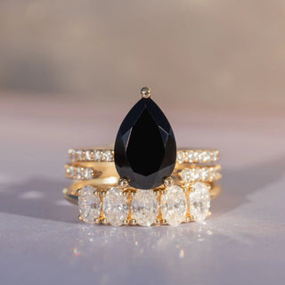 flat lay of black onyx pear engagement ring stacked with white diamond bands against a purplish gradient background