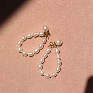 pearl drop earrings against a pink background