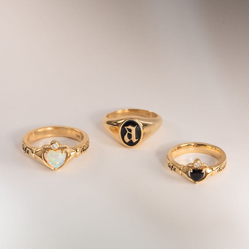 3 rings - two with heart shaped gemstones and one with initial enamel letter A against a beige bakcground