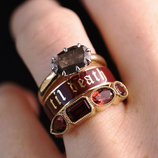 A close-up of a hand wearing a stack of three gothic-style rings. The top ring features a large smoky brown gemstone.