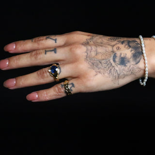 Tattooed hand wearing the Sapphire Sempre Ring and two Everyday Tear Drop Pearl Bracelets on a black background