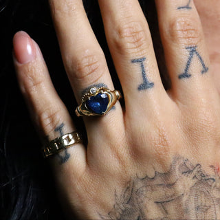 Tattooed hand wearing the blue heart Sapphire Sempre Ring and a gold band