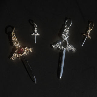 flat lay of 4 dagger charms, 2 silver nad 2 gold, on a black background