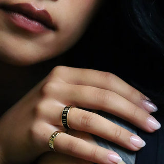 Tattooed hands wearing black enamel Til Death bands, another hand resting on the shoulder