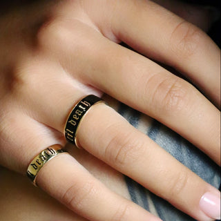 Tattooed hands wearing a black enamel Til Death band and the Til Death Gold Band