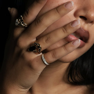 Hand near the face wearing a white enamel Til Death® band with black diamond stacking bands and a lab-created diamond Sempre ring