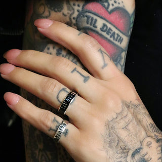 Hand wearing two Til Death bands, holding an arm with a til death heart tattoo