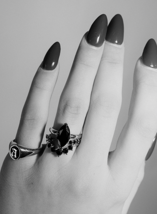 black and white photo of hand with two rings and painted nails on a plain background