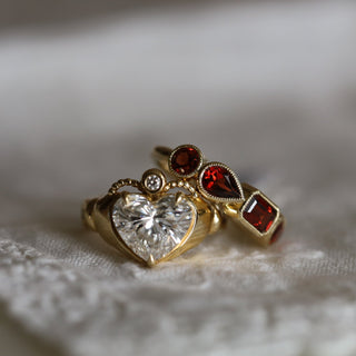 Gold ring with heart-shaped gemstone and red gemstones on a textured surface
