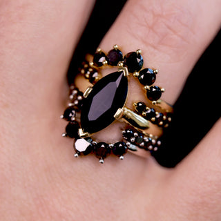 Gold ring with black gemstones on a finger against a dark background