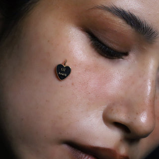 Til Death enamel heart charm held against the cheek, black heart with gold lettering