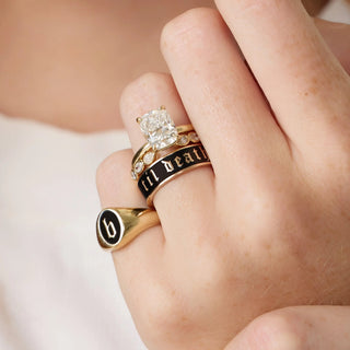 Hand wearing three gold rings with a diamond on a neutral background