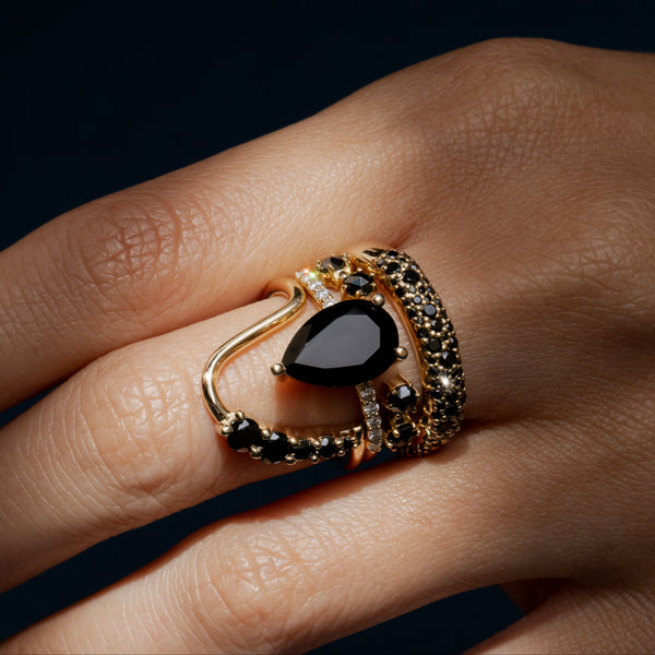 Gold ring with black gemstone on a finger against a dark background