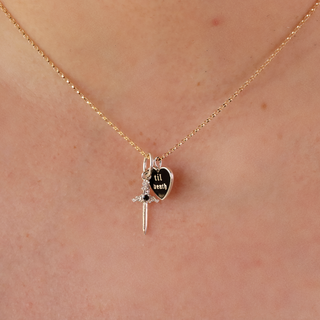 Gold necklace with a heart-shaped pendant and sword charm on a person's neck.
