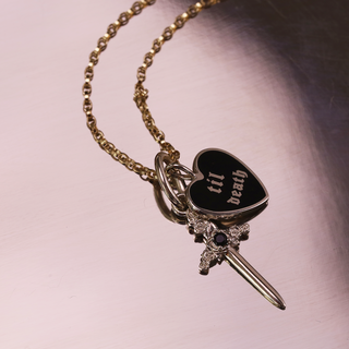 Heart-shaped pendant with a sword on a chain against a pink background