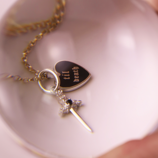Necklace with heart-shaped pendant and sword charm on a white dish