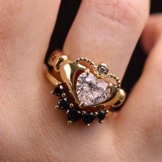 Gold ring with heart-shaped diamond and black gemstones on a finger