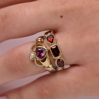 Gold ring with red gemstones on a person's finger against a light background