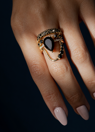 Gold ring with a black gemstone on a hand against a dark background