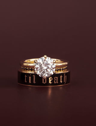 Gold ring with diamond and 'til death' band on a dark background