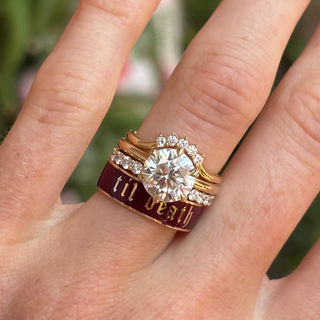 Gold ring with diamond and 'till death' engraving on a finger against a blurred green background