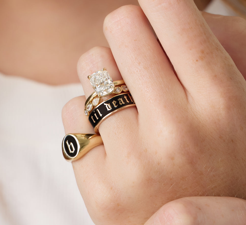 Hand wearing three gold rings with a diamond on a neutral background