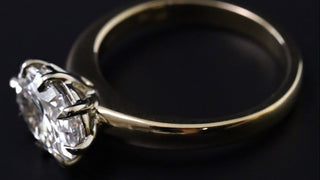 A close-up shot of a classic solitaire engagement ring featuring a large oval-cut clear gemstone in a silver-toned setting, mounted on a polished yellow gold band, set against a solid black background.
