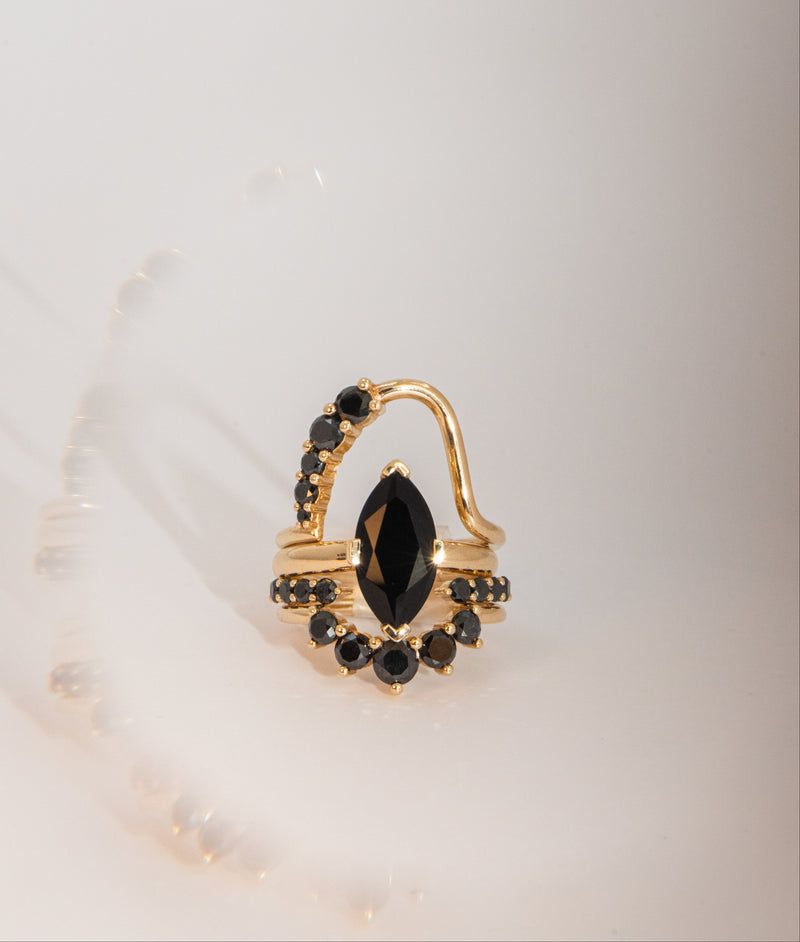 Gold rings with black gemstones stacked on top of each other, on a light background