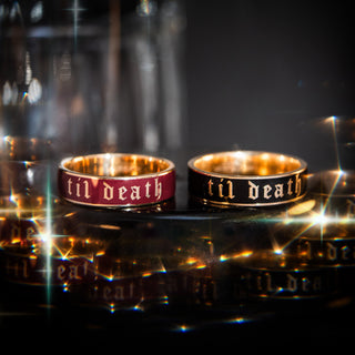 Two rings with 'til death' engraving on a reflective surface with blurred background