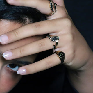 Woman with dark hair wearing the Black Diamond Cosmic Light Open Shank Band and an Initial Enamel Signet Ring against a dark background