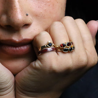 Woman resting her chin on her hands, wearing the 4mm Onyx Sempre Ring with other gold rings on a dark background