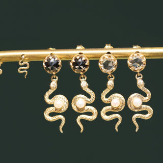Gold snake-shaped earrings with gemstones on a dark background
