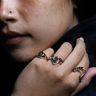 Hand wearing the yellow gold Initial Enamel Signet Ring with black diamond stacking bands, head resting on a dark surface