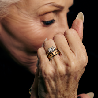 Close-up of an elderly woman's hand with a ring, against a dark background