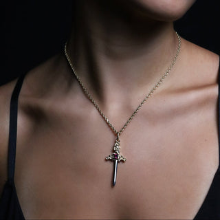 Large gold Cross My Heart dagger charm with a red garnet on a fine gold chain, dark background
