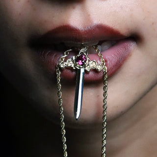 Large gold and garnet Cross My Heart dagger charm on a chain, held to the lips