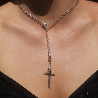 image of large gold dagger charm hanging on a silver chain on woman's neck