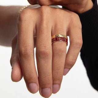 Hand wearing a ring with 'til death' engraving on a neutral background