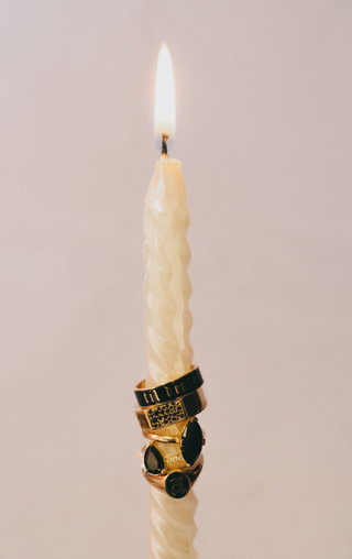 Candle with decorative black and gold rings on a plain background