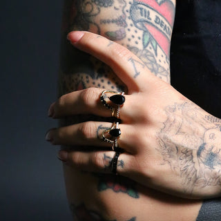 Tattooed hand wearing the Sweet Melissa and Mini Sweet Melissa black onyx pear rings on a dark background