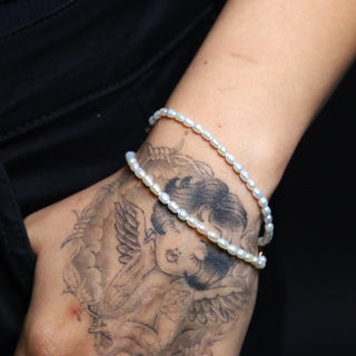 Tattooed hand in a pocket wearing two Everyday Tear Drop Pearl Bracelets