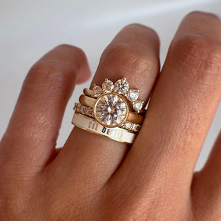 Hand wearing two gold rings with diamond accents on a white background
