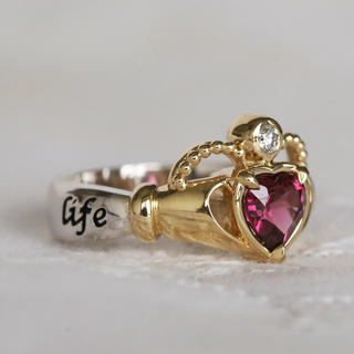 Gold ring with heart-shaped gemstone and 'life' engraving on a light background