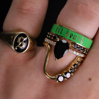 Close-up of a hand wearing two rings with intricate designs on a dark background