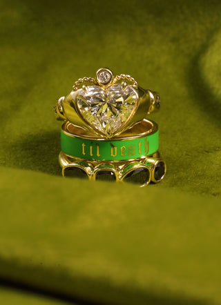 Gold ring with a large heart-shaped diamond and green band on a green fabric background