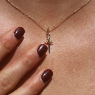 small gold dagger charm on chain, close up of woman's neck with hands reaching for it (wearing red nail polish)