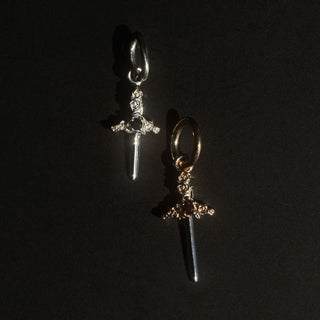 two small dagger charms on a black background (one sterling silver, the other gold)