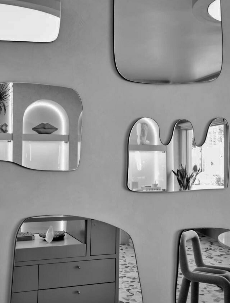 Wall with multiple abstract-shaped mirrors reflecting a room's interior.