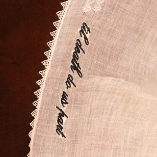 Embroidered text on a lace-trimmed fabric with a dark brown background